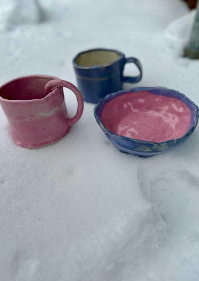 en lyserød kop, en lyseblå kop og en lyseblå og lyserød skål står i sne